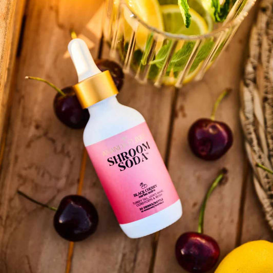 Shroom Soda Black Cherry bottle with cherries and a cocktail on a wooden surface