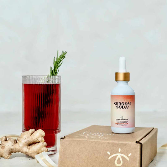 Shroom Soda bottle with a cranberry ginger drink and ginger root on a light background